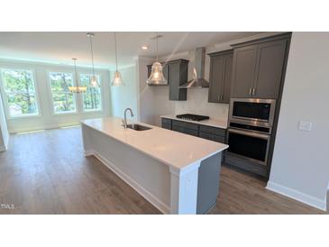 Modern kitchen boasts gray cabinets, stainless appliances, quartz counters, and hardwood flooring at 691 Bandon Aly, Cary, NC 27513