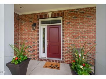 Charming brick home with a red front door and decorative potted plants on a sunny porch at 10310 Sablewood Dr # 111, Raleigh, NC 27617