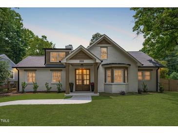 Charming white brick home featuring a manicured lawn, walkway, and a covered front porch with elegant wood accents at 2100 Summit St, Durham, NC 27707