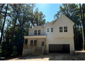 New two-story white home boasts an attached garage, covered porch with wooden railing and surrounded by mature trees at 701 Locust Ln, Raleigh, NC 27603