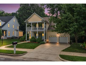 Charming yellow two-story home with double front porch and well-manicured lawn and a two-car garage at twilight at 10415 Ashmead Ln, Raleigh, NC 27614