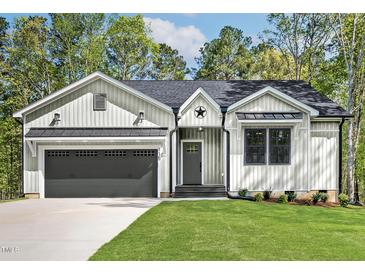 Charming home showcasing vertical siding, a two-car garage, and a well-manicured lawn at 205 Shawnee Dr, Louisburg, NC 27549