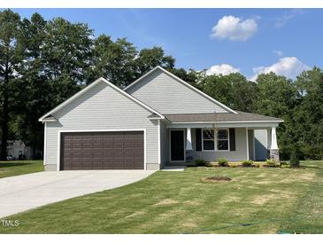 Charming single-story home featuring a front-facing garage and manicured lawn under a bright, cloud-dotted sky at 175 Oakfield Trace Dr, Four Oaks, NC 27524
