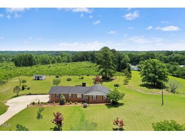 A ranch-style home with a brick facade, large front yard, mature trees, and a backdrop of lush greenery at 1035 Aquilla Rd, Benson, NC 27524