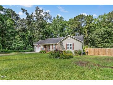 Charming single-story home with a well-maintained lawn, flower garden, and partial wooden fence under a blue sky at 229 White Oak Farm Dr, Willow Springs, NC 27592