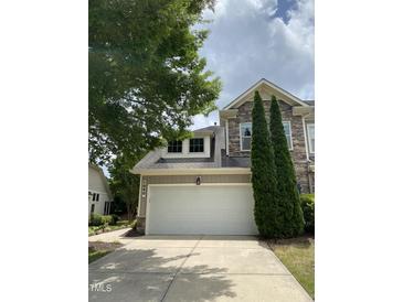 Stone and siding exterior with a white garage door, manicured lawn, and mature evergreens at 1090 Indigo Ridge Pl, Cary, NC 27519