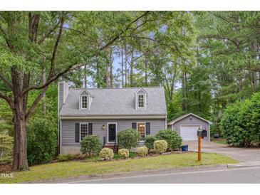 Charming cottage-style home with dormer windows, gray siding, lush landscaping, and a detached garage at 1302 Valley Run Dr, Durham, NC 27707