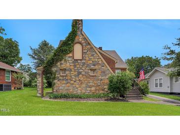 Charming stone and brick house with an American flag, beautiful lawn, and manicured landscaping at 407 Hillcrest Ave, Burlington, NC 27215