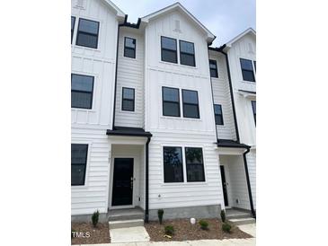 A bright exterior view of newly constructed townhomes with black trim and white siding at 3105 White Blossom Ct, Raleigh, NC 27610