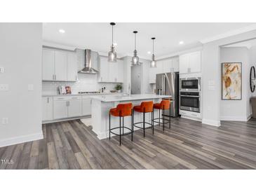 Bright kitchen features white cabinets, stainless steel appliances, a spacious island with pendant lighting and three orange chairs at 709 Emerald Bay Cir # 833, Raleigh, NC 27610
