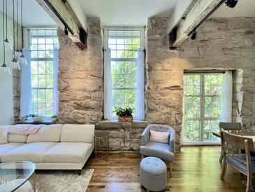 Bright living room featuring stone walls, hardwood floors, beamed ceilings, and lots of natural light from large windows at 1500 River Mill Dr # 310, Wake Forest, NC 27587