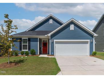 Charming single-story home with blue siding, a two-car garage, manicured lawn and bright red front door at 265 Purple Aster St, Youngsville, NC 27596
