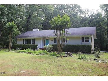 Charming single-story home with a lush green lawn, mature trees, and a lovely blue front door at 5112 Stephens Ln, Durham, NC 27712