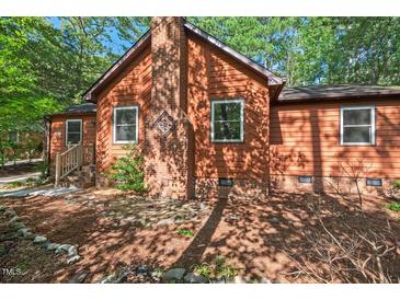 Cozy single-Gathering home featuring a brick chimney and brown siding, nestled amongst leafy trees at 5315 Mccormick Rd, Durham, NC 27713