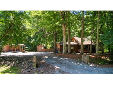 Charming log cabin nestled among mature trees with a gravel driveway and multiple outbuildings at 3263 S Jim Minor Rd Rd, Haw River, NC 27258
