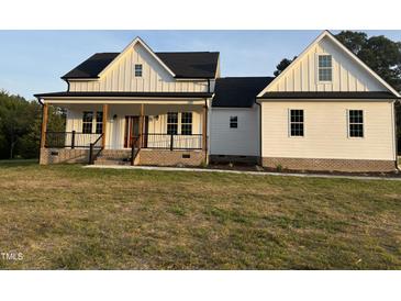 Charming white farmhouse-style home featuring a welcoming front porch with stylish black railings and brick accents at 50 Leah Ln, Louisburg, NC 27549