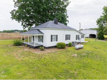 Charming white farmhouse with a metal roof and a spacious front yard surrounded by mature trees at 5004 Us 70 Alt, Princeton, NC 27569