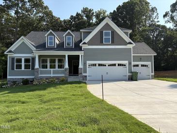 Two-story home with a two car garage, gray paint and stone accents, situated on a lawn with surrounding trees at 78 Mineral Springs Way, Benson, NC 27504