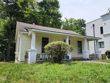 Charming yellow home featuring a covered porch, cozy front yard, and lush surrounding greenery at 1106 Fargo St, Durham, NC 27707