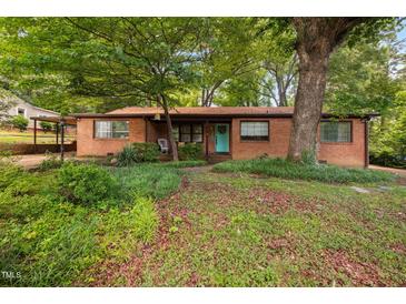 Charming brick home featuring a vibrant blue front door and mature trees in a spacious yard at 1120 E Oak Dr, Durham, NC 27712