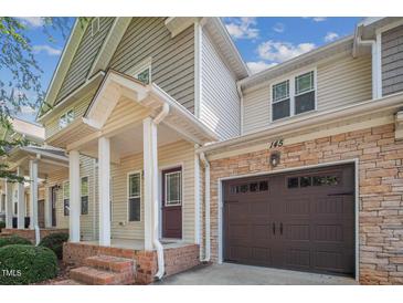 Charming townhouse featuring a stone facade, brown garage door, and covered front porch with brick steps at 145 Mariah Towns Way, Garner, NC 27529