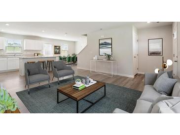 Bright open-concept living room featuring modern gray furniture, hardwood floors, and seamless flow to the kitchen at 16 Powder Ct, Angier, NC 27501