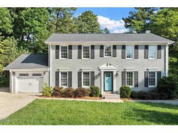 Charming two-story brick home with a manicured lawn, gray roof, black shutters, and a delightful blue front door at 5509 Cliffwood Ct, Raleigh, NC 27609