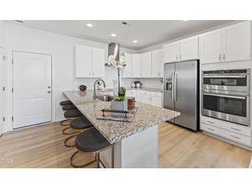 Modern kitchen features white cabinets, stainless steel appliances, and a granite-topped island with bar stool seating at 915 Ball Field Aly # 101, Cary, NC 27511