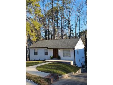 Charming one-story home with a white painted brick exterior, landscaped yard, and a walkway leading to the front entrance at 1128 E Geer St, Durham, NC 27704