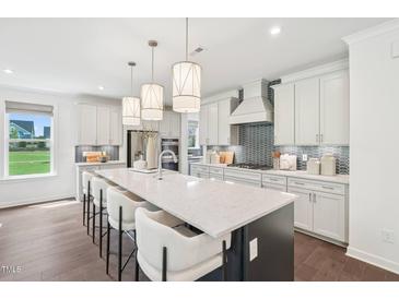 Bright kitchen boasts a large island with seating, modern lighting, and stainless steel appliances at 45 Shady Creek Way, Fuquay Varina, NC 27526