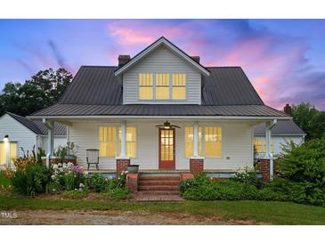 Charming home featuring a metal roof, inviting front porch, and beautiful landscaping at 6318 Hurdle Mills Rd, Roxboro, NC 27574
