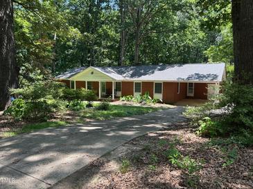 Charming red brick single story home with covered porch, set amongst a densely treed and landscaped front yard at 1225 Fairlane Rd, Cary, NC 27511