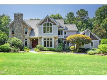 Beautiful two-story home featuring a stone chimney, large windows, a manicured lawn, and mature landscaping at 267 Bald Eagle Dr, Pittsboro, NC 27312