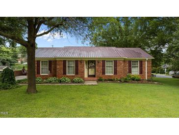 Charming brick home with a metal roof, complemented by a lush green lawn and mature trees at 516 Ivey Rd, Graham, NC 27253