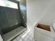 Modern shower features sleek gray tiling and a mosaic-tiled shower floor and a white sink and cabinet below at 4905 Hidden Pasture Way, Zebulon, NC 27597