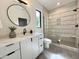 Modern bathroom showcasing a round mirror, white vanity, and a glass-enclosed shower with tiled walls at 5208 Knollwood Rd, Raleigh, NC 27609
