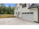 Long, concrete driveway leading to a two-car garage of a white home surrounded by green grass and trees at 225 Whistlers Cv, Louisburg, NC 27549