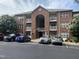 Red brick three-story condo building with arched entrance and white balcony railings in a landscaped parking lot at 129 Sturbridge Dr # 15, Clayton, NC 27520
