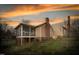 Back of the home with a screened-in porch, brick chimney and lush lawn against a colorful sunset sky at 2416 Glencoe St, Burlington, NC 27217