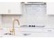 Close-up of a white kitchen with a stainless hood, gold hardware, and light tile backsplash at 240 Fast Pitch Ln, Four Oaks, NC 27524