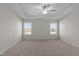 Bright bedroom featuring a tray ceiling, ceiling fan, plush carpet, and two windows offering scenic views at 585 Husketh Rd, Youngsville, NC 27596