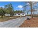 Exterior view of a manufactured home with an expansive gravel driveway surrounded by mature trees at 1235 Schloss Rd, Louisburg, NC 27549