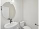 Compact powder room with a round mirror and white pedestal sink and toilet at 909 Montague Ave, Durham, NC 27703