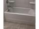 Clean bathroom with a bright white tub and modern fixtures, complemented by neutral tile flooring at 1600 Maelyn Way, Fuquay Varina, NC 27526