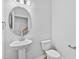 Neat half-bathroom with a modern pedestal sink, a round mirror, and a white toilet, showcasing minimalist design at 2750 Lacy Holt Rd, Graham, NC 27253