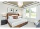 This bedroom features tray ceilings, a large window, a brown leather headboard, and minimalist artwork at 2308 Beeblossom Pl, Fuquay Varina, NC 27526