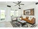 Cozy living room with a leather sofa, accent chairs, a ceiling fan, and large windows overlooking the backyard at 2308 Beeblossom Pl, Fuquay Varina, NC 27526