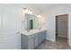 A bathroom features gray cabinetry, dual sinks, large mirror, modern lighting, tile flooring, and white door at 587 Glenkirk Pl, Garner, NC 27529