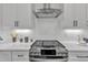 Modern kitchen featuring stainless steel stove with sleek range hood, white cabinets, and stylish backsplash at 1000 Addison Pl # 101, Raleigh, NC 27610