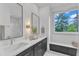 Bathroom featuring double sinks, stylish mirrors, and a window bench with forest views at 1000 Addison Pl # 102, Raleigh, NC 27610